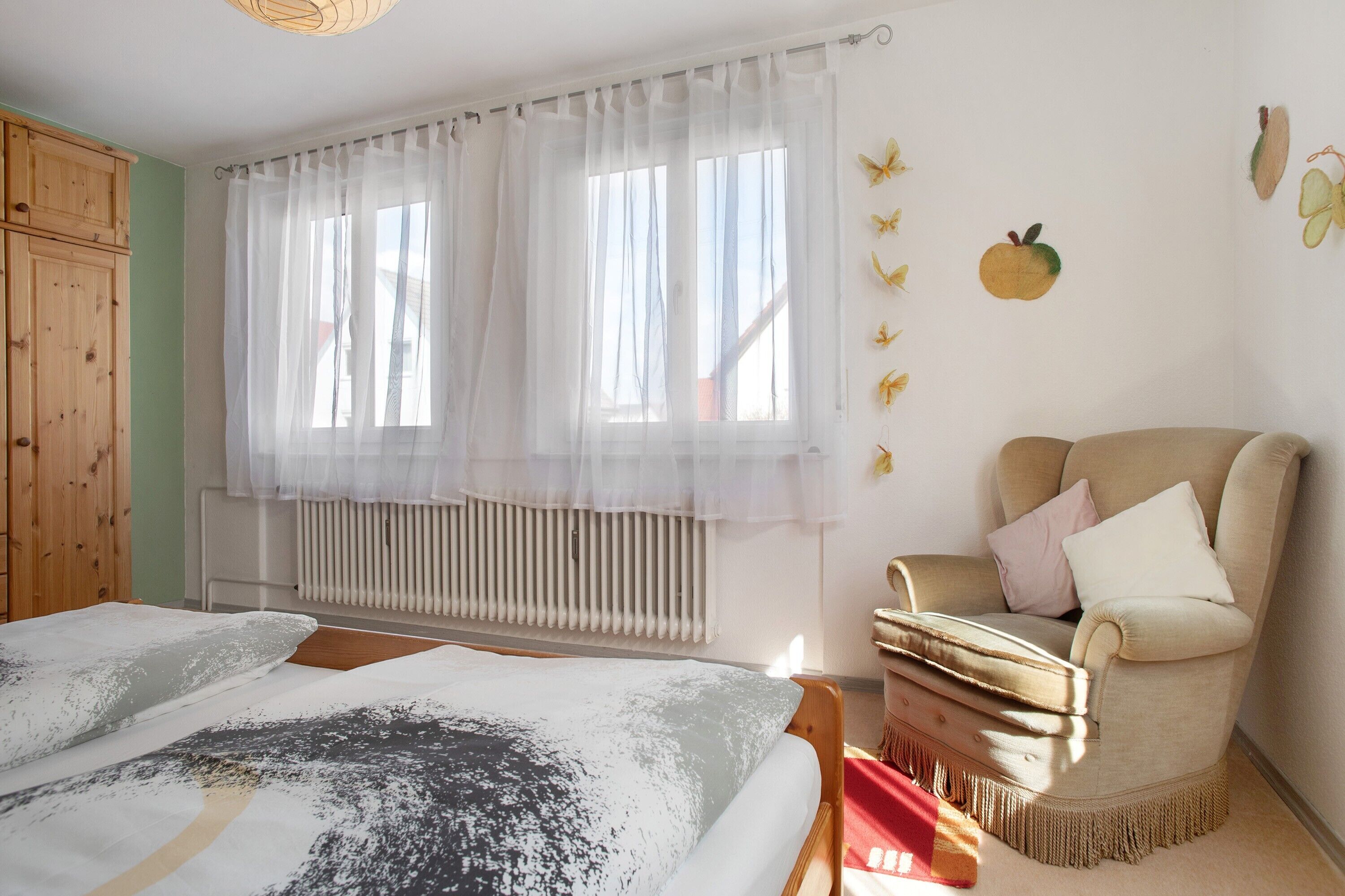 Een slaapkamer met een bed, een stoel, een radiator en een raam met gordijnen.