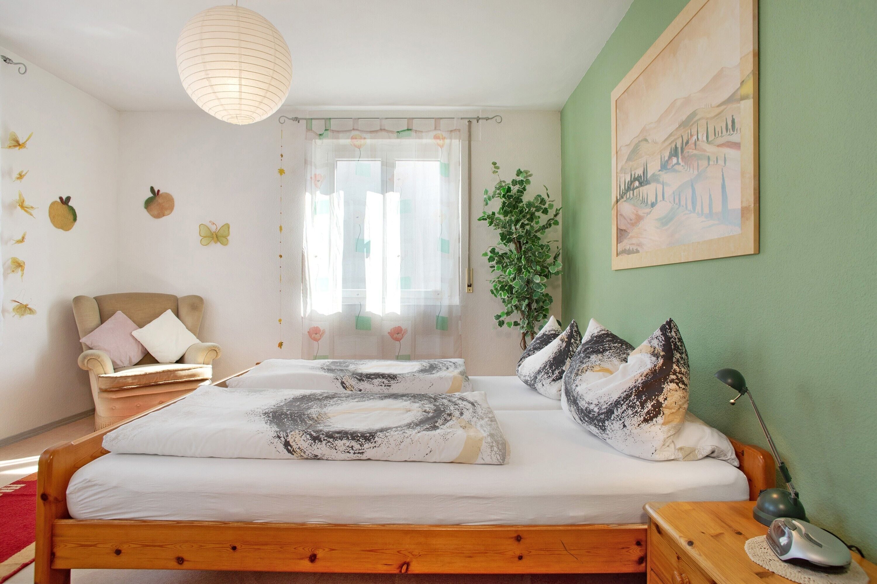 A bedroom with a wooden bed, a chair, a desk with a lamp, and a painting on the wall.
