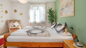 Ein Schlafzimmer mit einem Holzbett, einem Sessel, einem Schreibtisch mit Lampe und einem Bild an der Wand.
