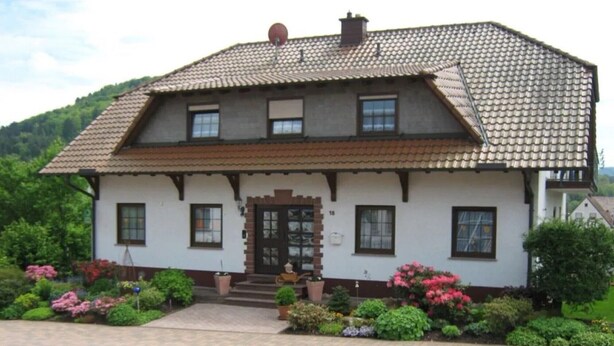 A two-story house with a tiled roof, a front door, and a small porch. - Apartment 'Sonnenblick - Fewo 1' with Balcony and Wi-Fi (Fischbach bei Dahn)