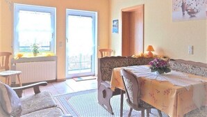 A dining area with a table set for two, a chair, a radiator, and a door leading outside. - Apartment 'Sonnenblick - Fewo 1' with Balcony and Wi-Fi (Fischbach bei Dahn)
