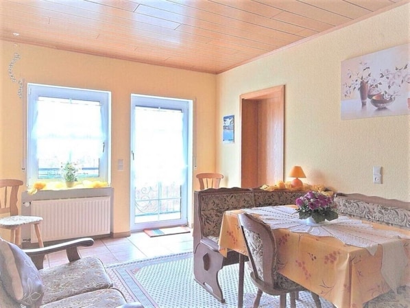 A dining area with a table set for two, a chair, a radiator, and a door leading outside.