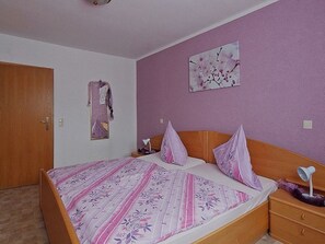 Ein Schlafzimmer mit Bett, Holz-Kopfteil, Nachttischen, einem Wandspiegel und einem floralen Gemälde.