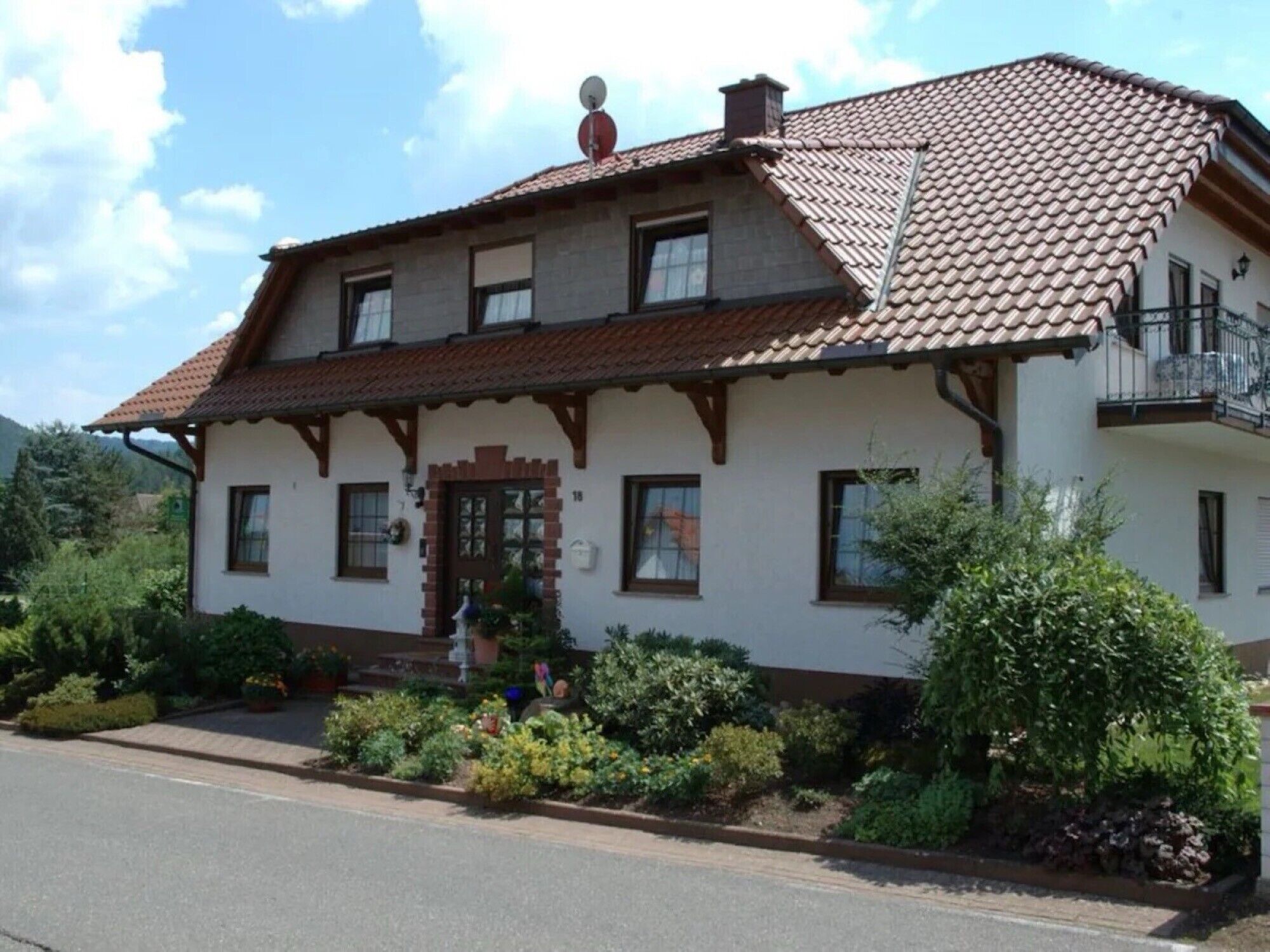 A two-story house with a tiled roof, a front porch with steps, and a small garden area.
