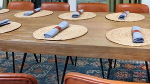 Un coin repas avec une table en bois, des sets de table en fibres tressées et des chaises orange.