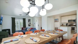 Un salon moderne comprenant une table à manger pour six personnes, un coin cuisine et un espace détente avec un canapé et des fauteuils.
