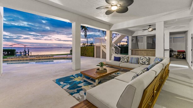 A spacious living area with a large window overlooking a pool and a beach at sunset. - Luxury Beachfront Retreat~Pool~Game Room~Sleeps 16 (Bradenton)