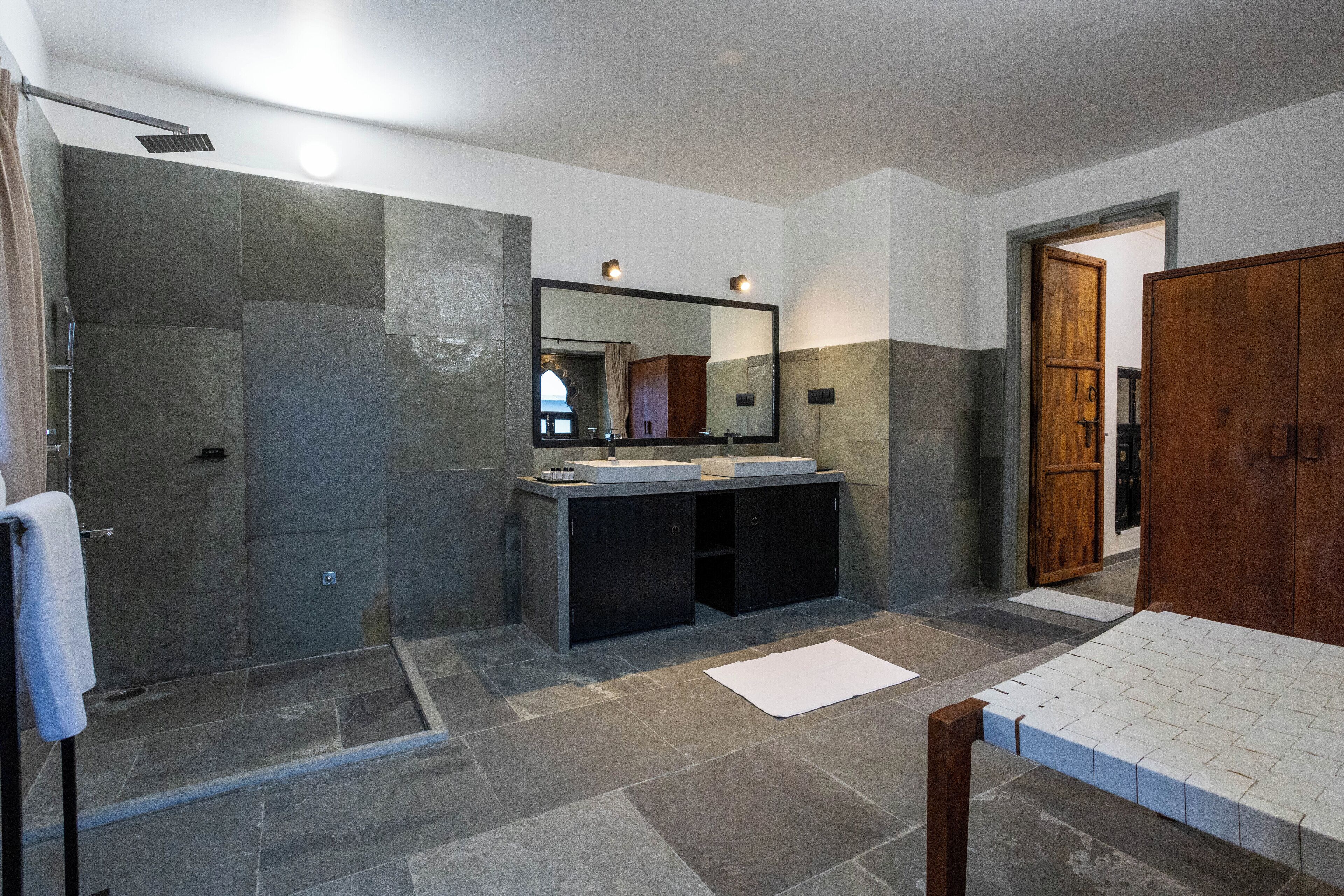 A modern bathroom with a large mirror, two sinks, a shower area, and a wooden wardrobe.