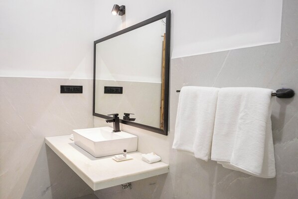 Un baño moderno con un lavabo blanco, un espejo grande y un perchero para toallas.