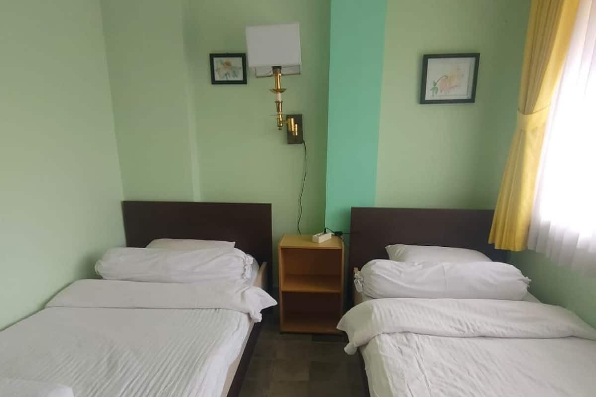 Ein Hotelzimmer mit zwei Einzelbetten, einem Nachttisch, einer Wandlampe und einem Fenster mit Vorhängen.