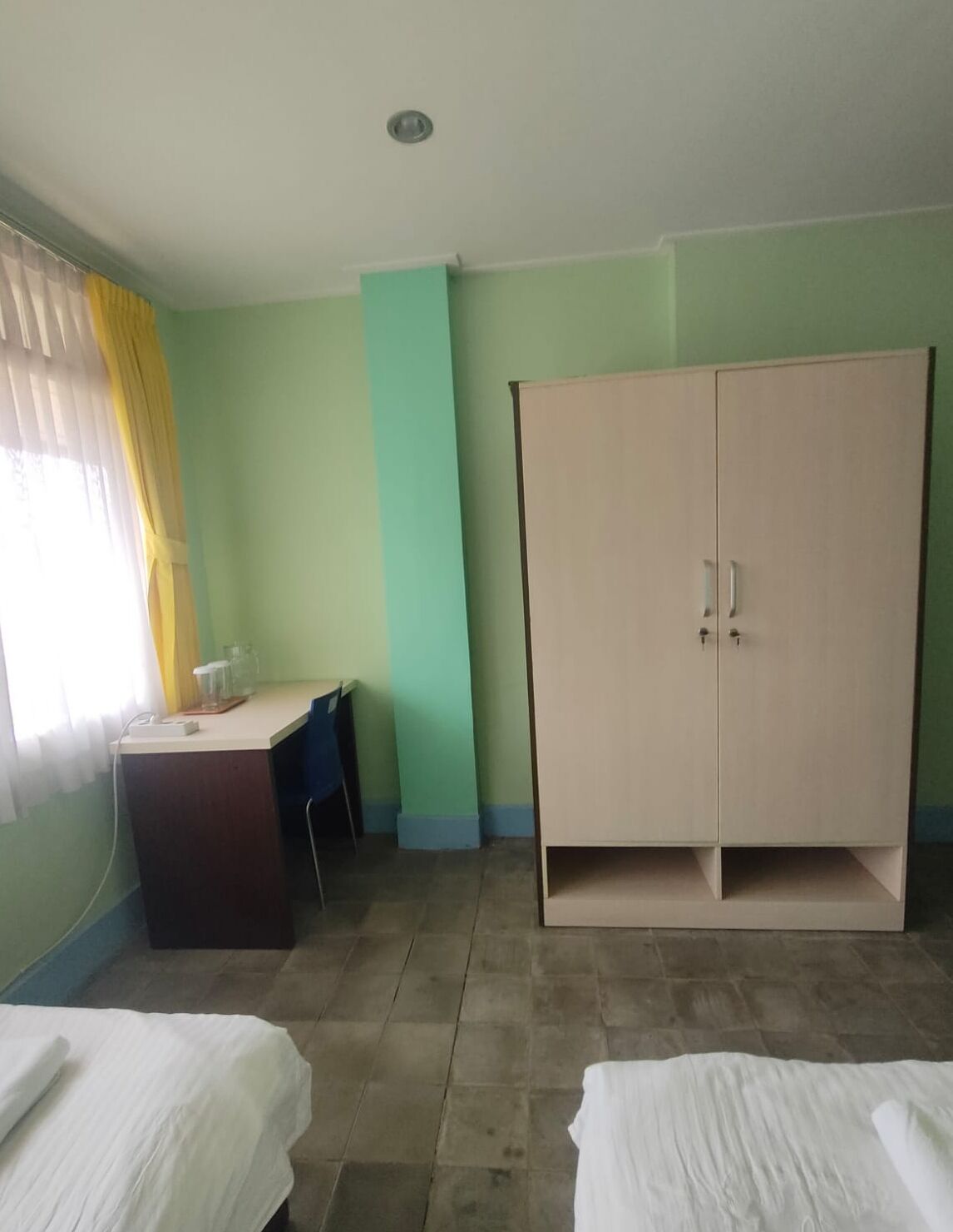 Une chambre avec un bureau, deux lits, une armoire et une fenêtre avec des rideaux.