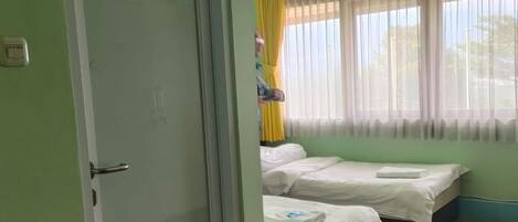 A room with two beds, a door, and a window with curtains.