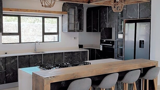 Una cocina moderna con una isla central, taburetes de bar y un refrigerador empotrado.