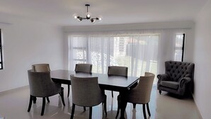Un comedor amplio con una gran mesa y seis sillas, un sillón capitonado y una lámpara moderna.