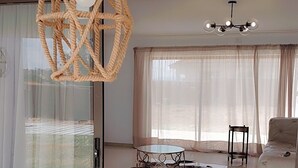 Una sala de estar moderna con un separador de vidrio, un sofá blanco, una mesa de centro redonda y una lámpara colgante.