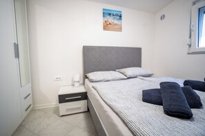 A bedroom with a bed, pillows, a nightstand, a lamp, and a window. - Villa Skundric (Vir)