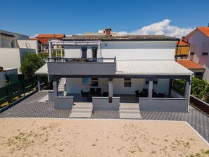 A two-story building with a flat roof, a covered outdoor seating area, and a staircase leading to the upper level. - Villa Skundric (Vir)