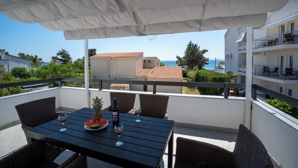 A balcony with a table set for two, featuring a bottle of wine, a glass, a pineapple, and a watermelon. - Villa Skundric (Vir)