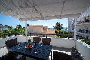 A balcony with a table set for two, featuring a bottle of wine, a glass, a pineapple, and a watermelon.