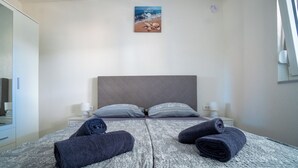 A neatly made bed with rolled towels, a headboard, and a wall-mounted picture of a beach scene. - Villa Skundric (Vir)