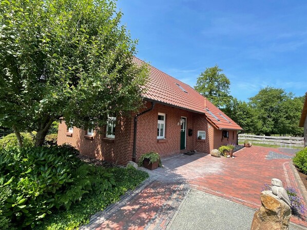 A brick building with a red-tiled roof, a paved driveway, and a garden area with a statue.