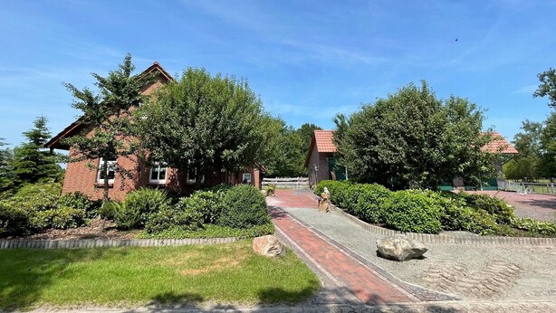 A brick house with a red roof, surrounded by green trees and a gravel pathway. - Apartment 'Uhlenhoff Boyken' with Private Terrace, Shared Garden and Wi-Fi (Apen-Bokelermoor)