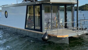 A modern houseboat with a covered deck, large windows, and a small outdoor seating area. - Houseboat 'Kitilou' with Lake View, Private Terrace, and Wi-Fi (Dobin)
