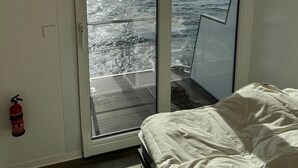 A room with a bed, a fire extinguisher, and a sliding glass door leading to a balcony with a view of a body of water. - Houseboat 'Kitilou' with Lake View, Private Terrace, and Wi-Fi (Dobin)