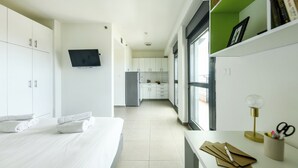 Une chambre d’hôtel moderne, équipée d’un lit, d’un bureau avec une lampe et offrant une vue sur la cuisine et l’espace de vie.