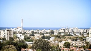 Un paysage urbain côtier avec une haute cheminée imposante, des immeubles résidentiels denses et une vue sur la mer.