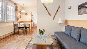 Un saló modern amb un sofà, taula de dinar, cadires, taula de centre amb flors, una làmpada i una obra d'art a la paret.