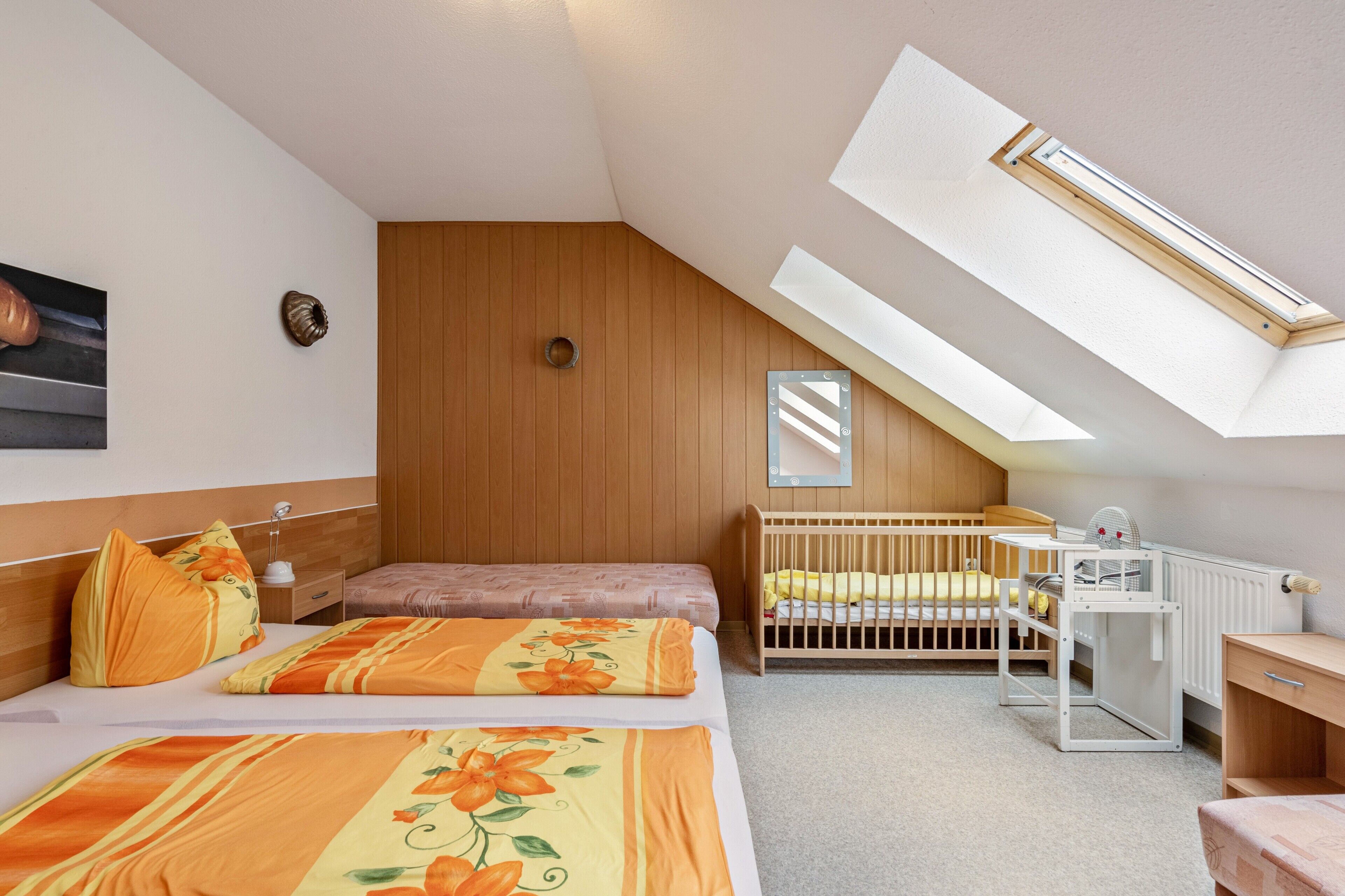 A bedroom with a sloped ceiling, a crib, a desk, and a radiator.
