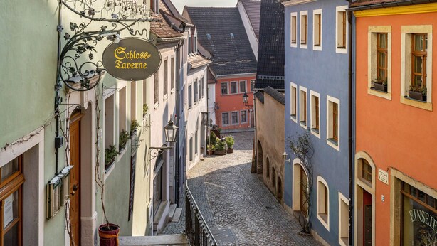 A narrow cobblestone street between buildings with a sign for 'Schloss Tavern'.