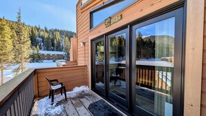 A wooden cabin with a large sliding glass door, a deck with a chair, and a snowy landscape in the background. - Key Condo 2934a (Keystone)