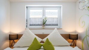 A bedroom with a bed, two bedside lamps, a window with curtains, and a vase with flowers. - Apartment '303' with Shared Garden, Wi-Fi and Air Conditioning (Hagnau)