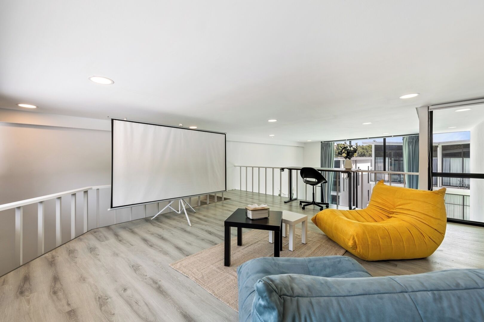 A modern room with a large screen, a yellow bean bag, and a blue couch.