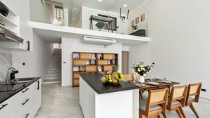 Une cuisine moderne dotée d’un îlot central, d’étagères en bois et d’un coin repas avec une table dressée pour quatre personnes.