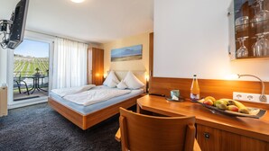 Una habitación de hotel con una cama, un escritorio con fruta, una botella y un cuadro.