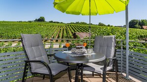 Una terraza con mesa y sillas, un paraguas amarillo y vistas a un viñedo.