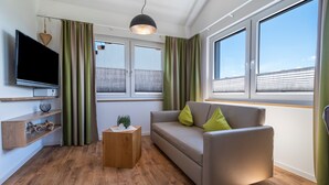 A modern living room with a sofa, a TV, a wooden coffee table, and a window with curtains. - Apartment '302' with Shared Garden, Wi-Fi and Air Conditioning (Hagnau)
