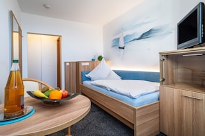 Una habitación de hotel con una cama, un televisor, un frutero, una botella y un cuadro en la pared.