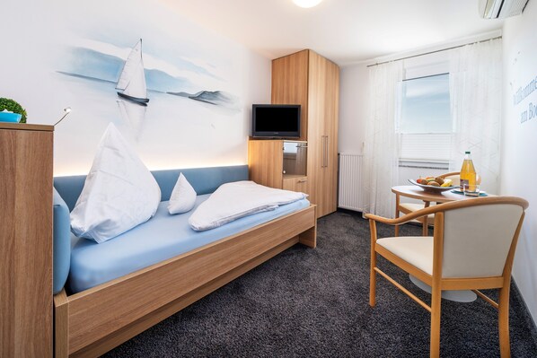 A room with a bed, a TV, a small table with a chair, and a window. - Room '104' with Shared Garden, Wi-Fi and Air Conditioning (Hagnau)