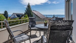 A balcony with outdoor furniture, a potted plant, and a view of the sea and mountains.