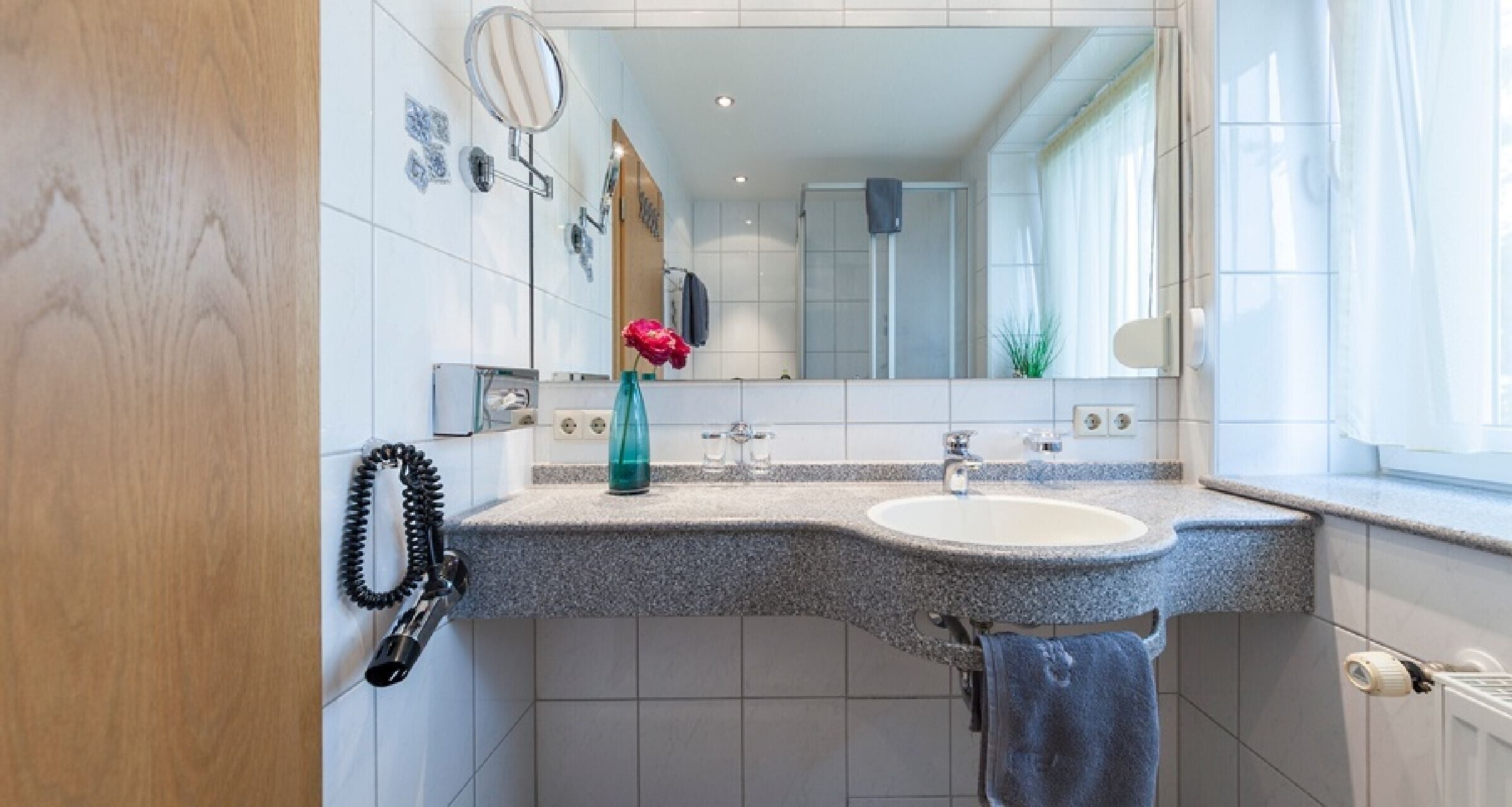 A bathroom with a granite countertop, a sink, a mirror, a towel rack, and a shower area.