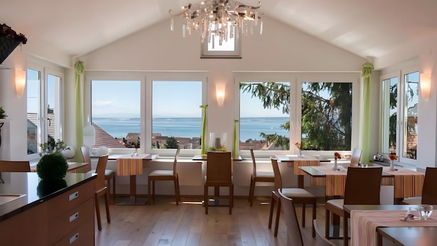 A spacious dining area with large windows, a chandelier, and a view of the ocean. - Room '205' with Shared Garden, Balcony and Wi-Fi (Hagnau)