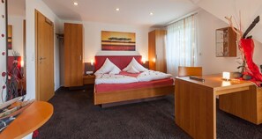 Quarto de hotel moderno com cama, mesas de cabeceira, escrivaninha e um quadro na parede.