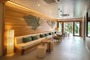 Un área de estar moderna con una pared de madera, un sofá con cojines verdes, sillas de mimbre y una lámpara de pie.