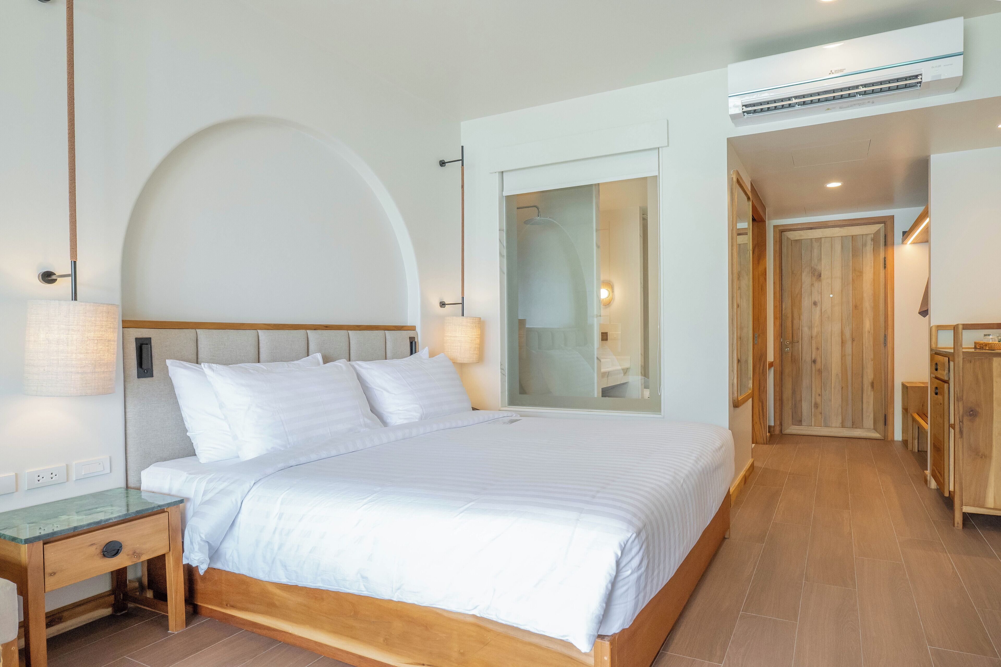A modern bedroom with a large bed, a bedside table, a lamp, and an air conditioning unit.
