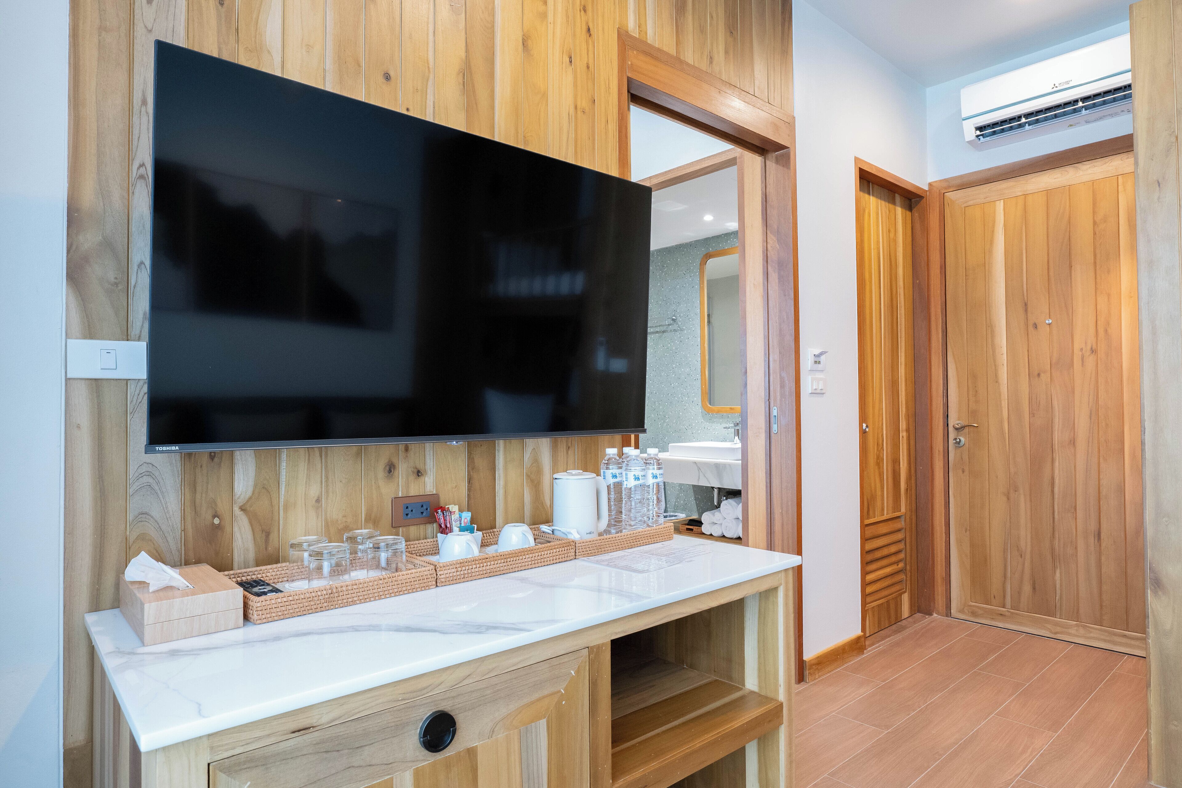Un baño moderno con un espejo grande, tocador de madera y televisor de pantalla plana.