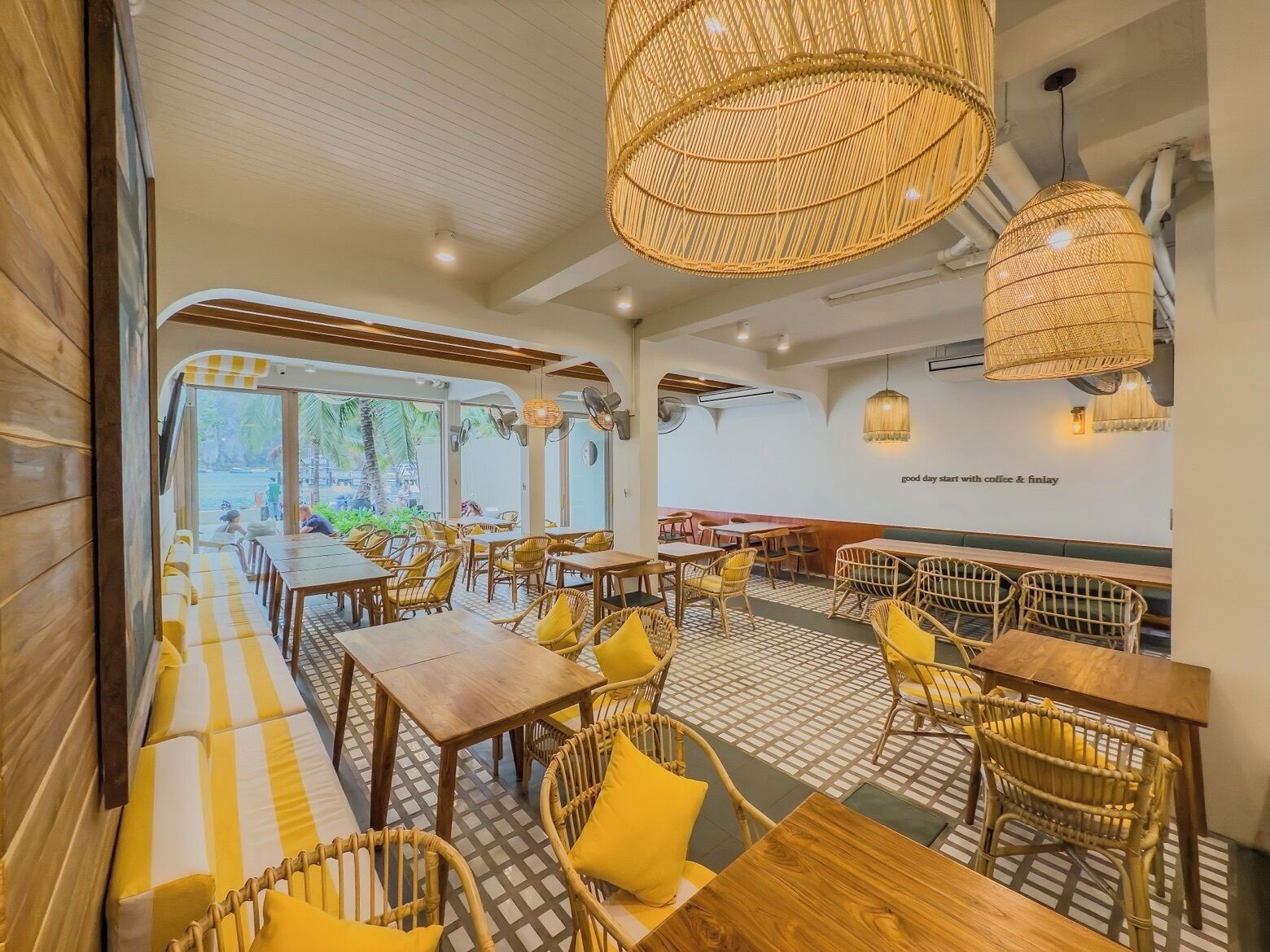 A restaurant with wooden furniture, yellow cushions, and woven light fixtures.